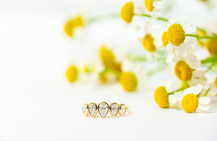 Gold ring with pear-shaped diamonds on a white background with yellow flowers.