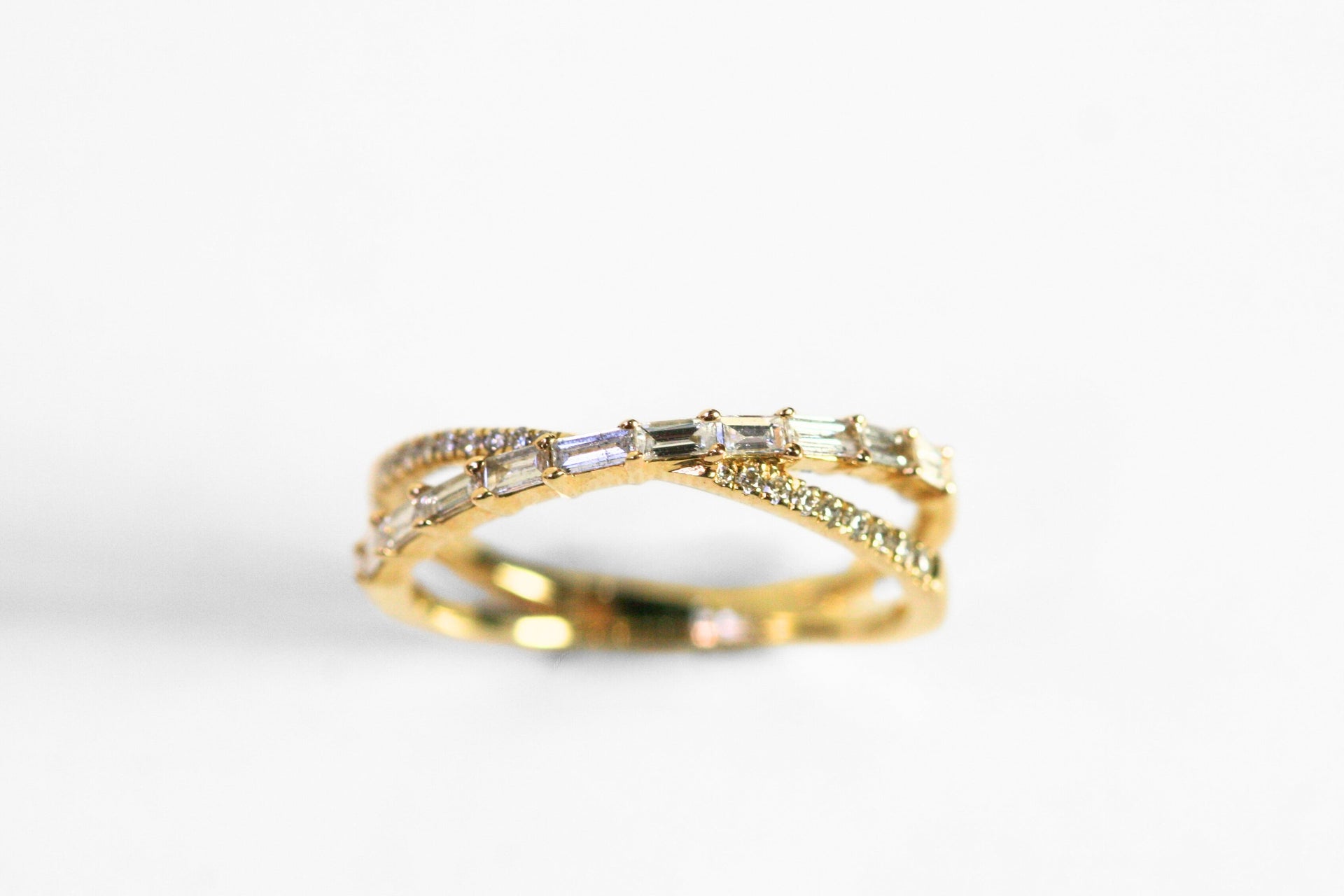 Ring shaped like an X. One arm of the X has round, brilliant cut diamonds. The other has horizontal baguettes. Set in yellow gold.