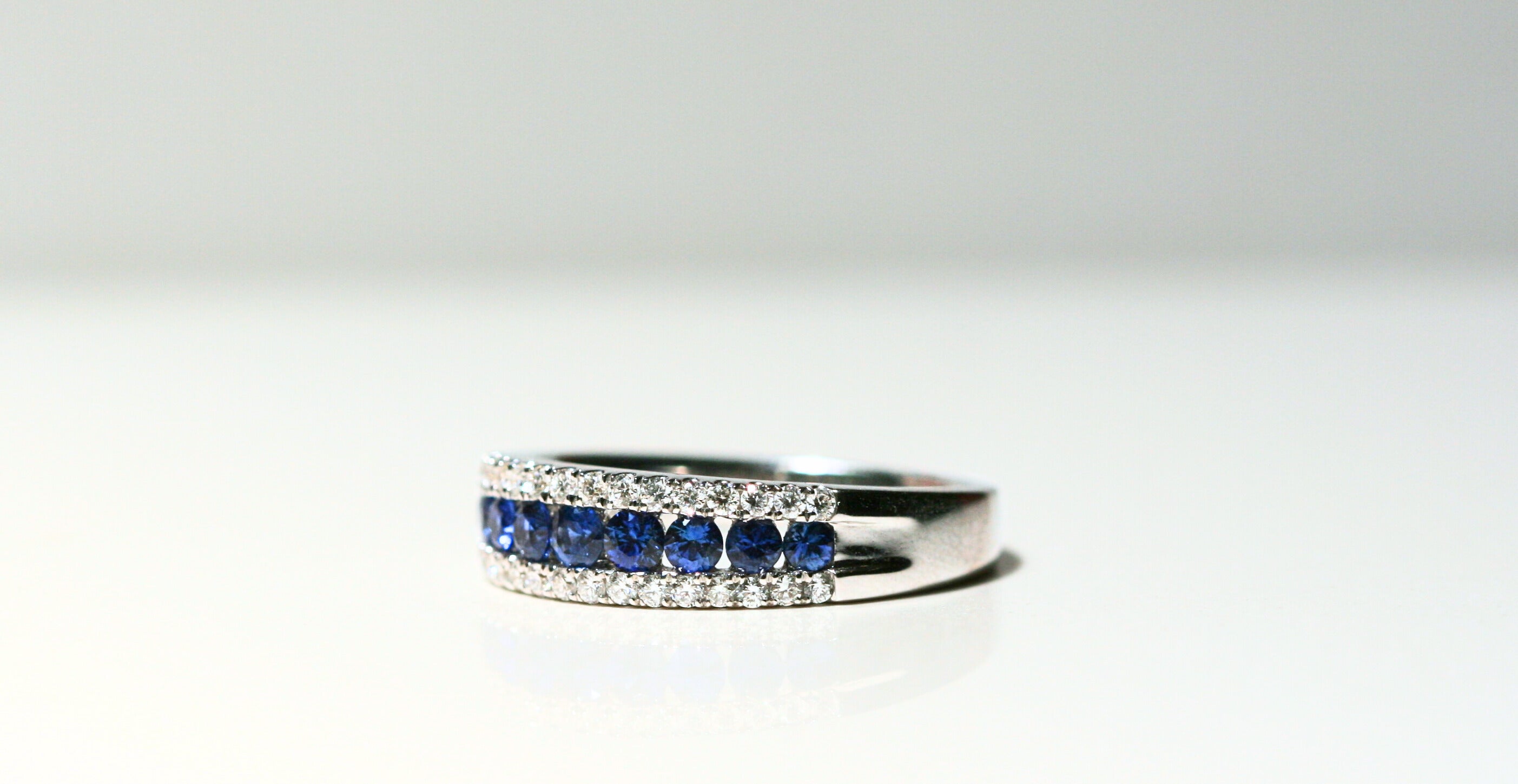 A white gold ring set with white diamonds and deep blue round sapphires. The sapphires look as though they're floating between the diamonds. The back of the ring is solid white gold. Local SF jewelry, San francisco, Luxury, hand made, Bay area, gift for her, gift for him.
