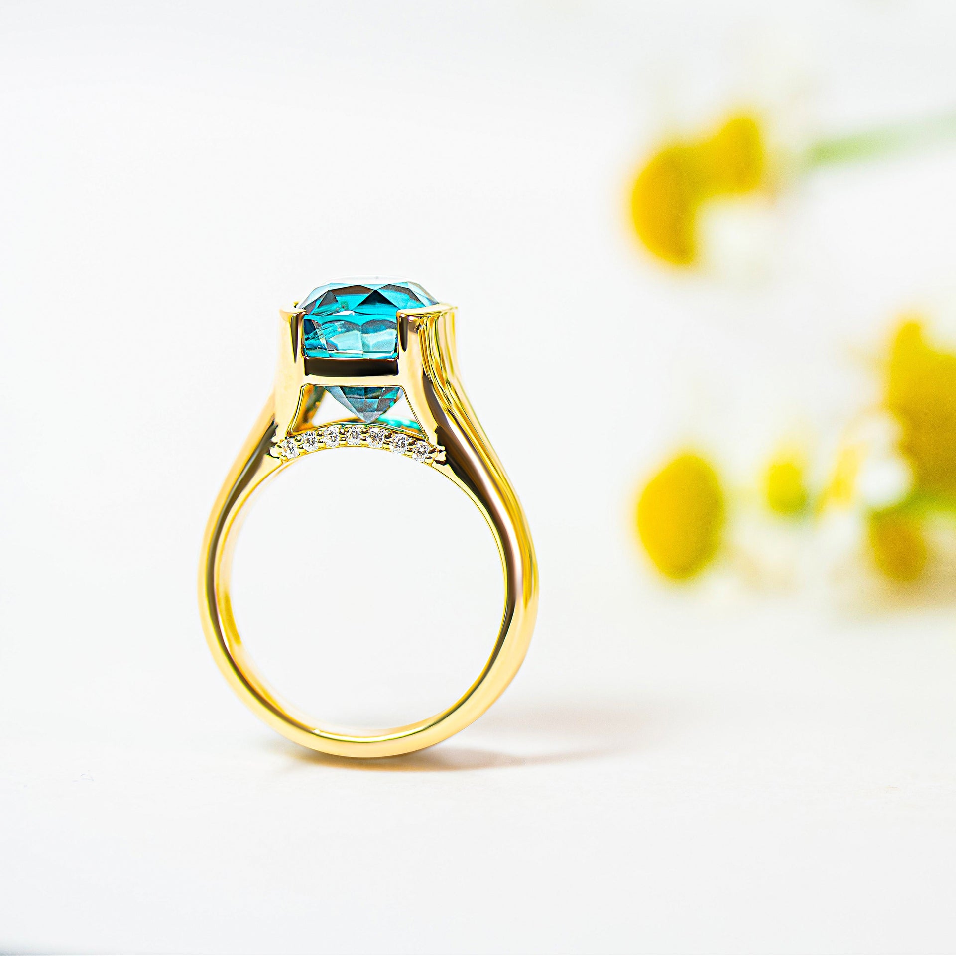 Gold ring with a blue zircon and diamonds on a white background with yellow flowers