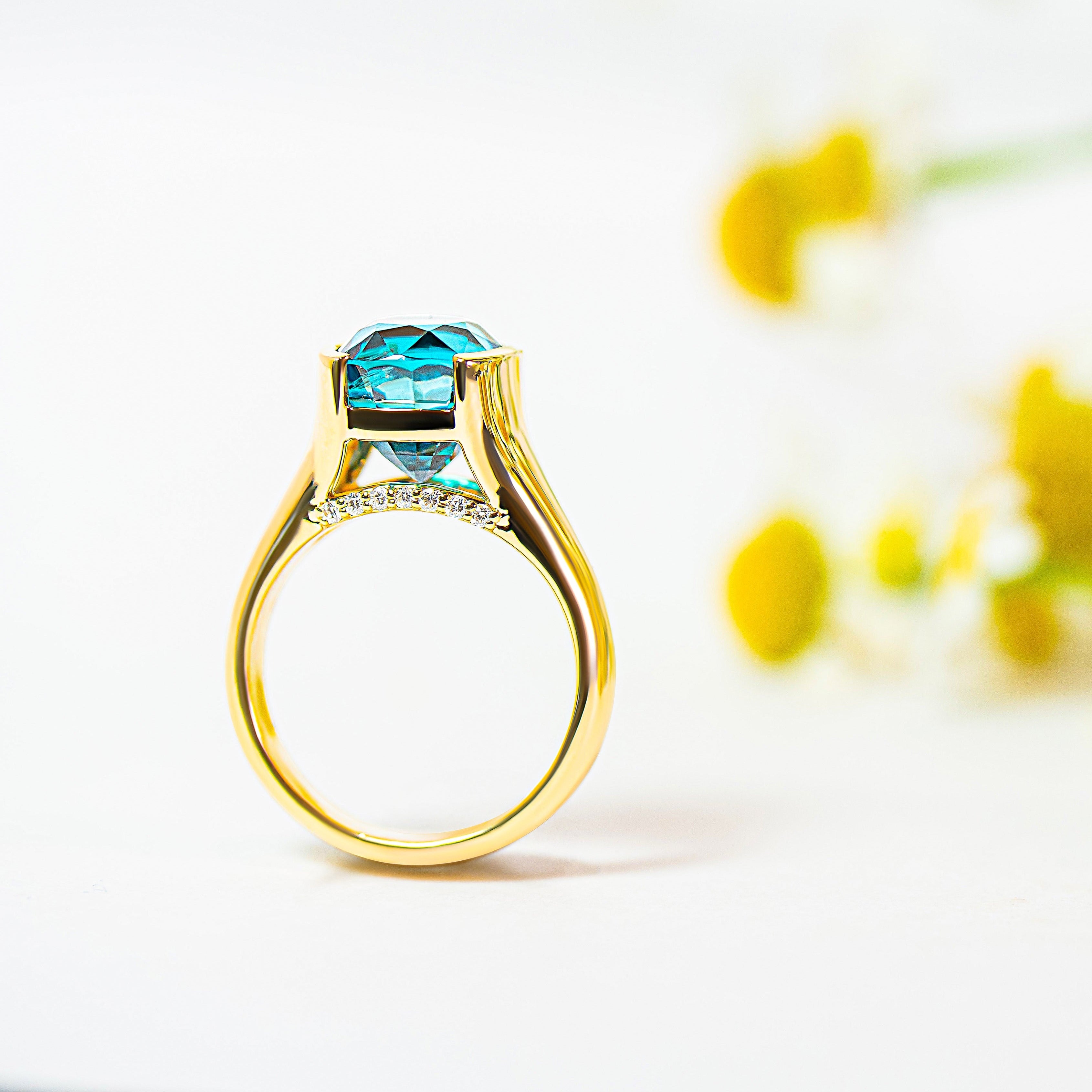 Gold ring with a blue zircon and diamonds on a white background with yellow flowers