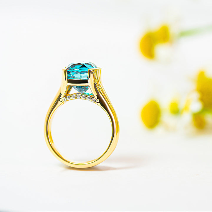 Gold ring with a blue zircon and diamonds on a white background with yellow flowers