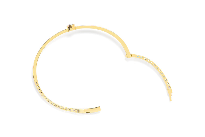 Top view of open gold bracelet with a tear-drop or pear shaped diamond on a white background