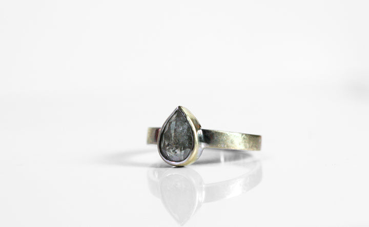 Pear shaped salt & pepper diamond is bezel set in white gold. The band is thick and has a hammered finish.