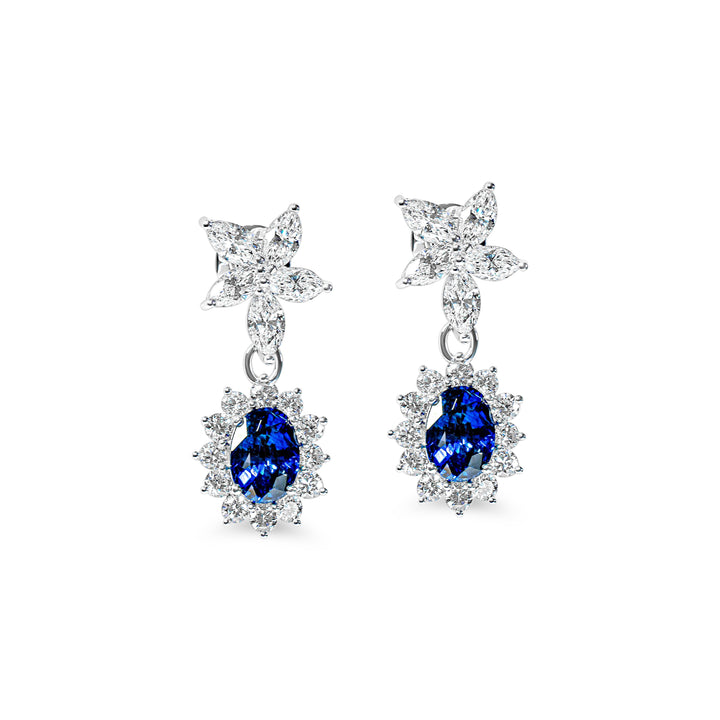 Pair of earrings with blue sapphires and flower-shaped designs on a white background