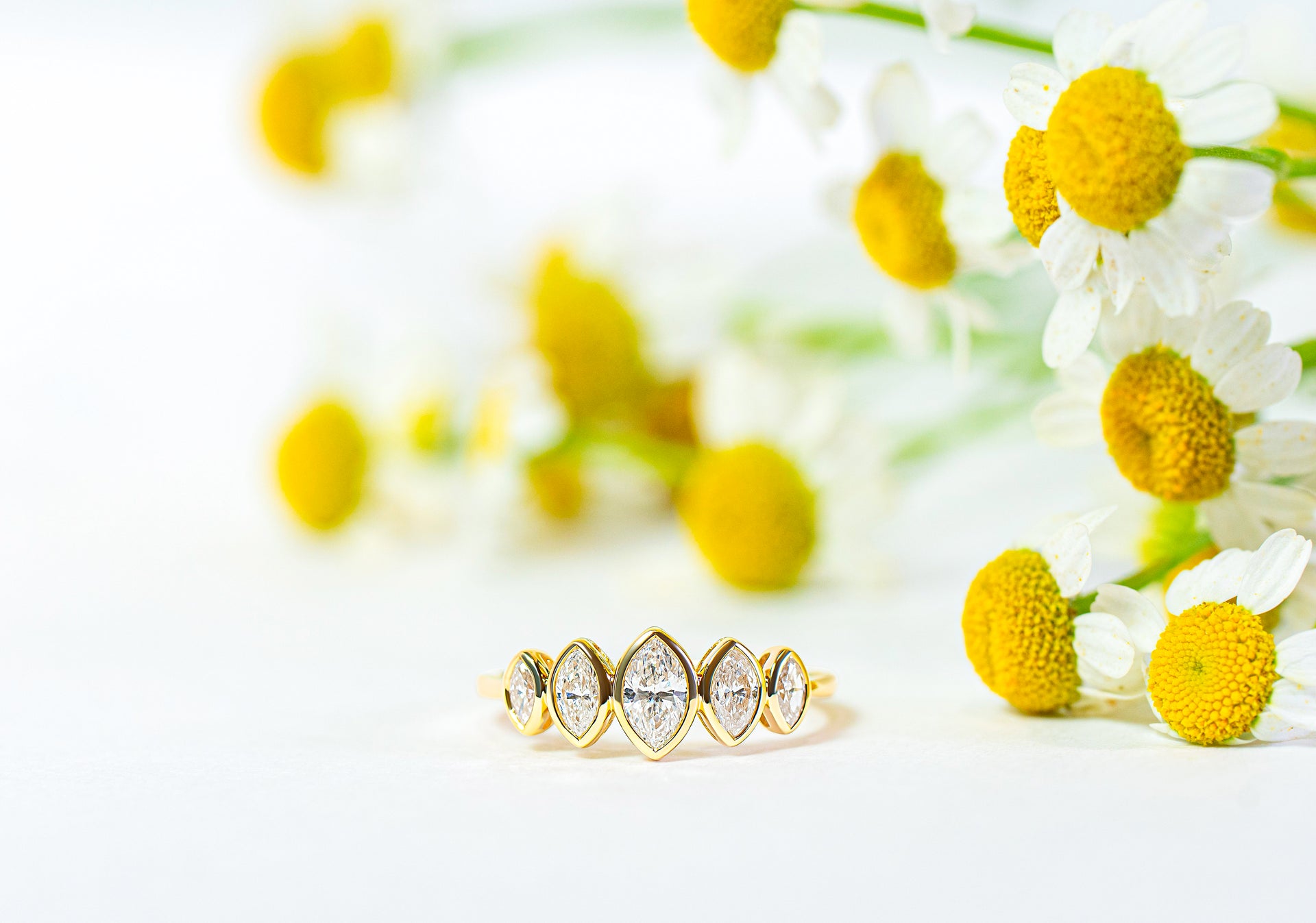 Gold ring with five marquise diamonds on a white background with yellow flowers