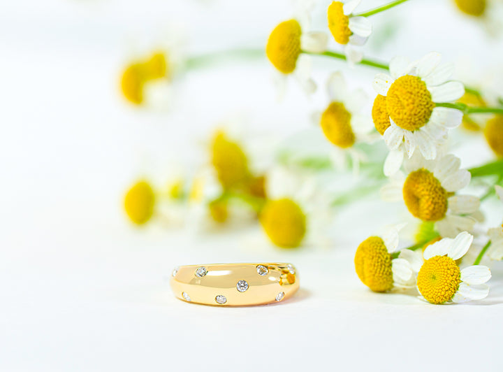 Gold ring with embedded diamonds on a white background with yellow and white flowers.