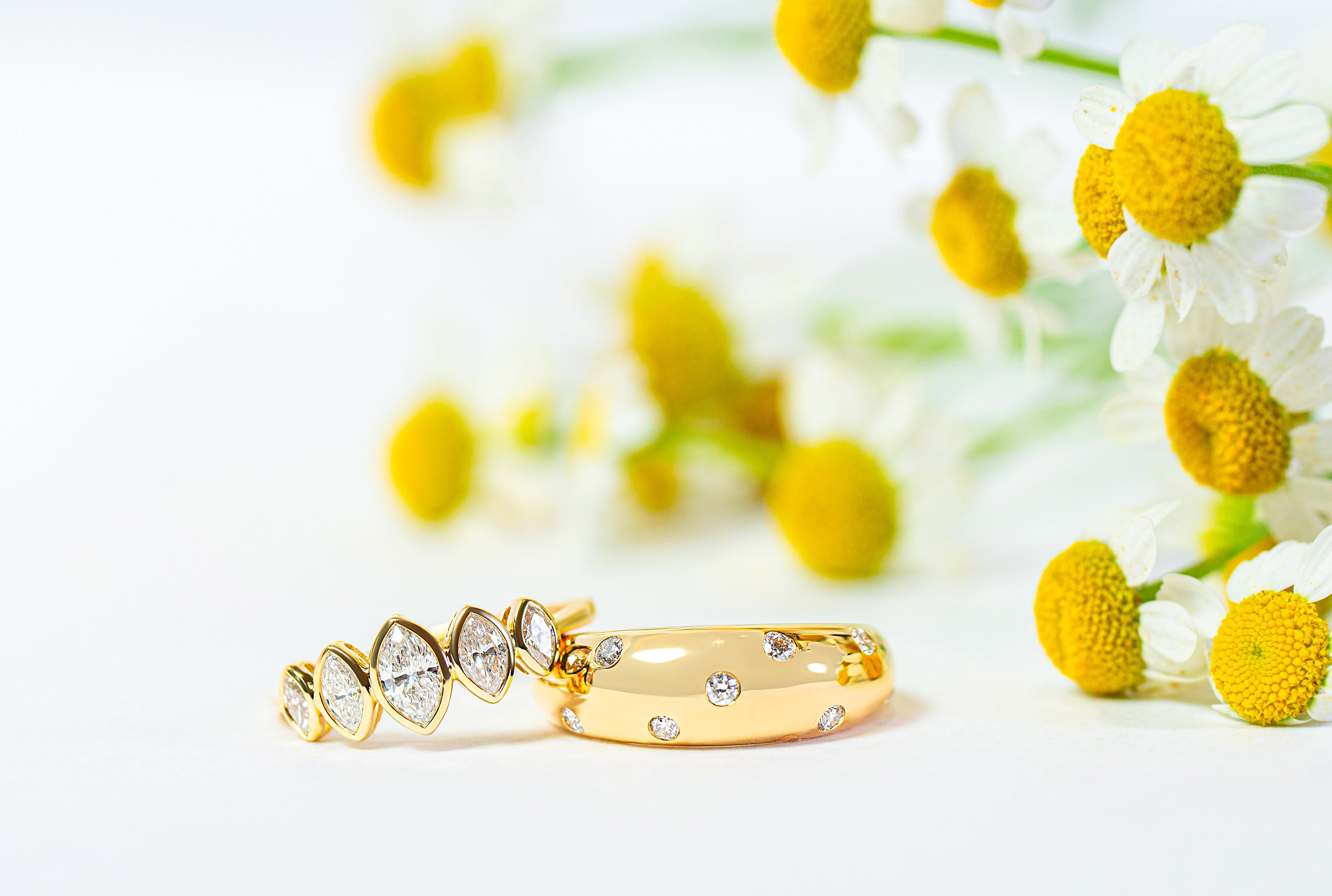 Two gold rings with diamonds on a white background with yellow flowers