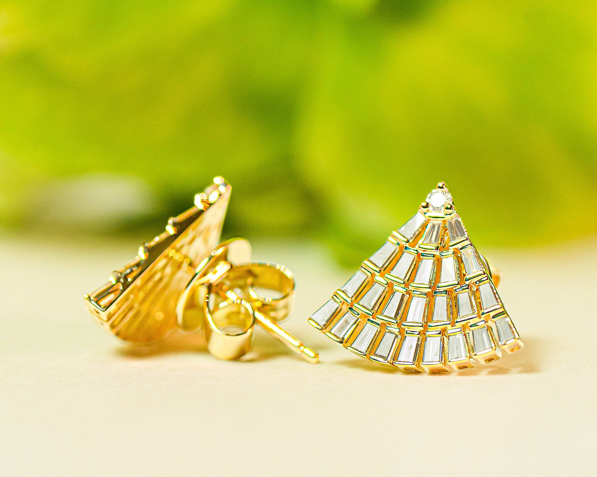 Gold fan-shaped earrings with diamonds on a light background