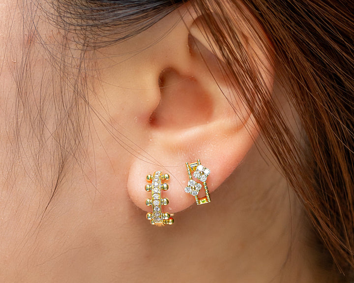Close-up of a person's ear wearing a pair of gold hoop earrings adorned with small round diamonds. 