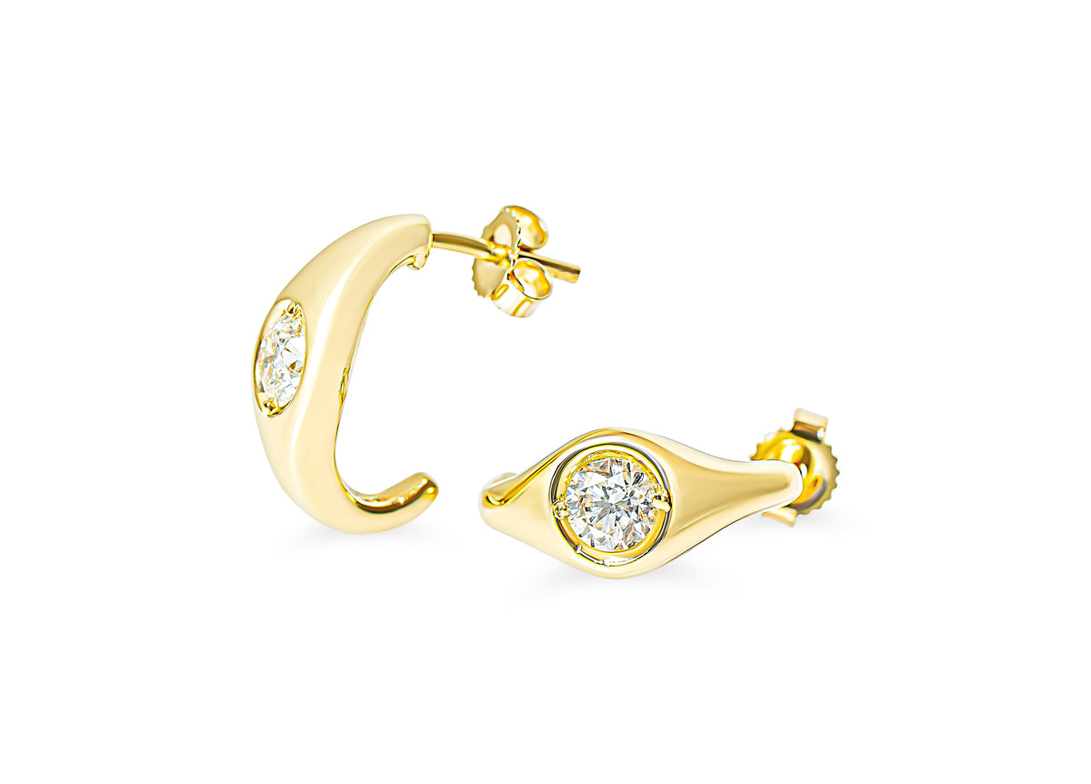 A pair of gold crescent-shaped stud earrings with a single round diamond flush set in the center, displayed on a clean white background.