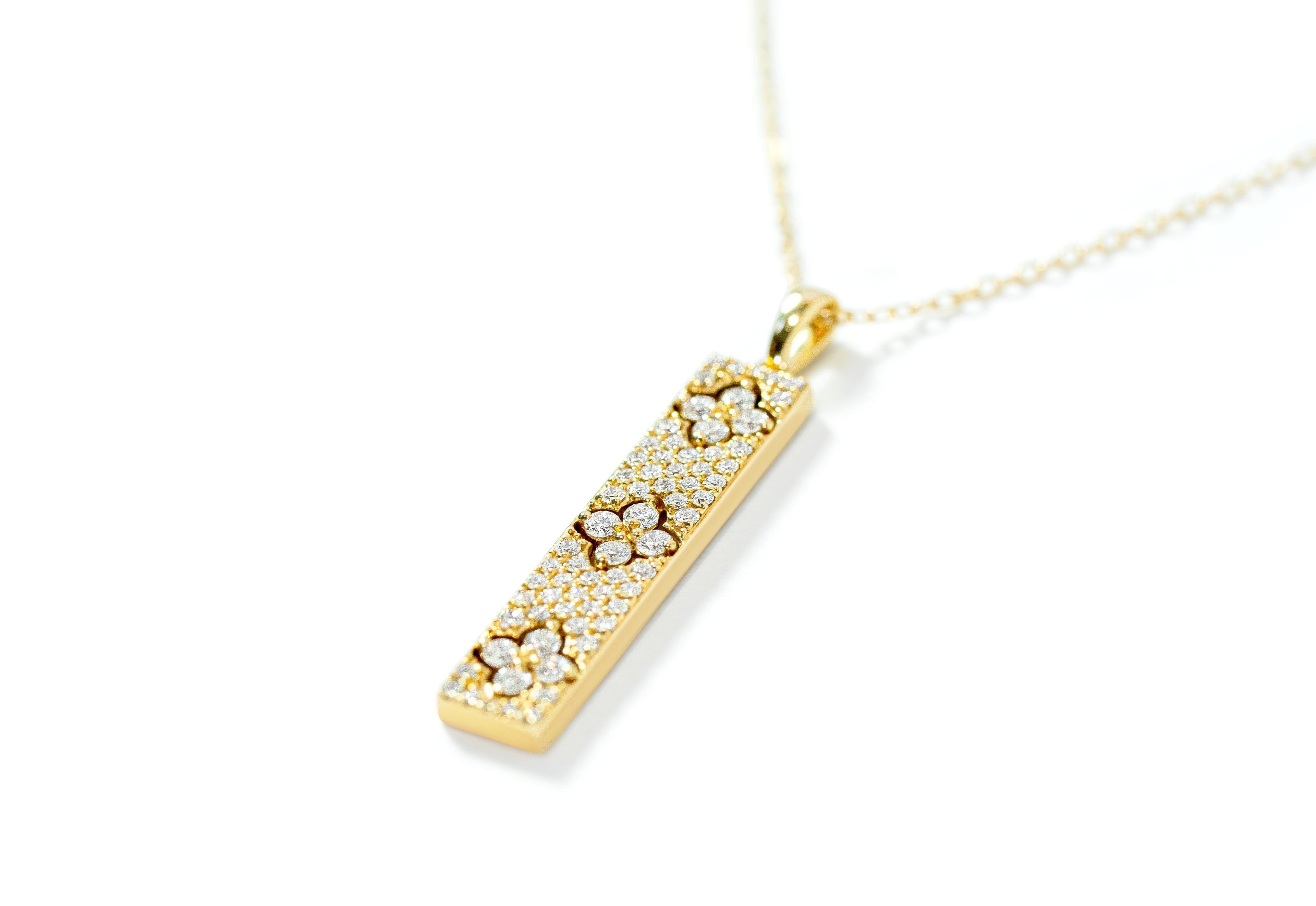 Gold bar necklace with a diamond pave pendant on a white background 