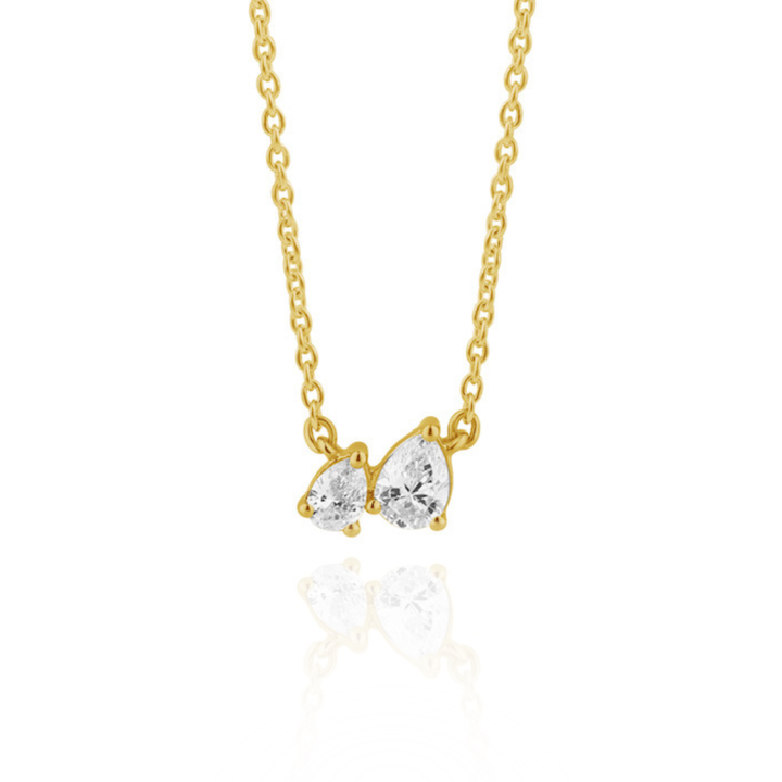 A gold chain necklace with a pendant featuring two off-set, pear-cut diamonds in a gold setting, shown against a plain white background.