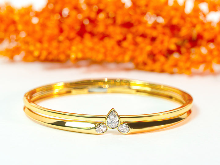 Two stacked gold bangles with diamond accents on a white background with orange leaves.