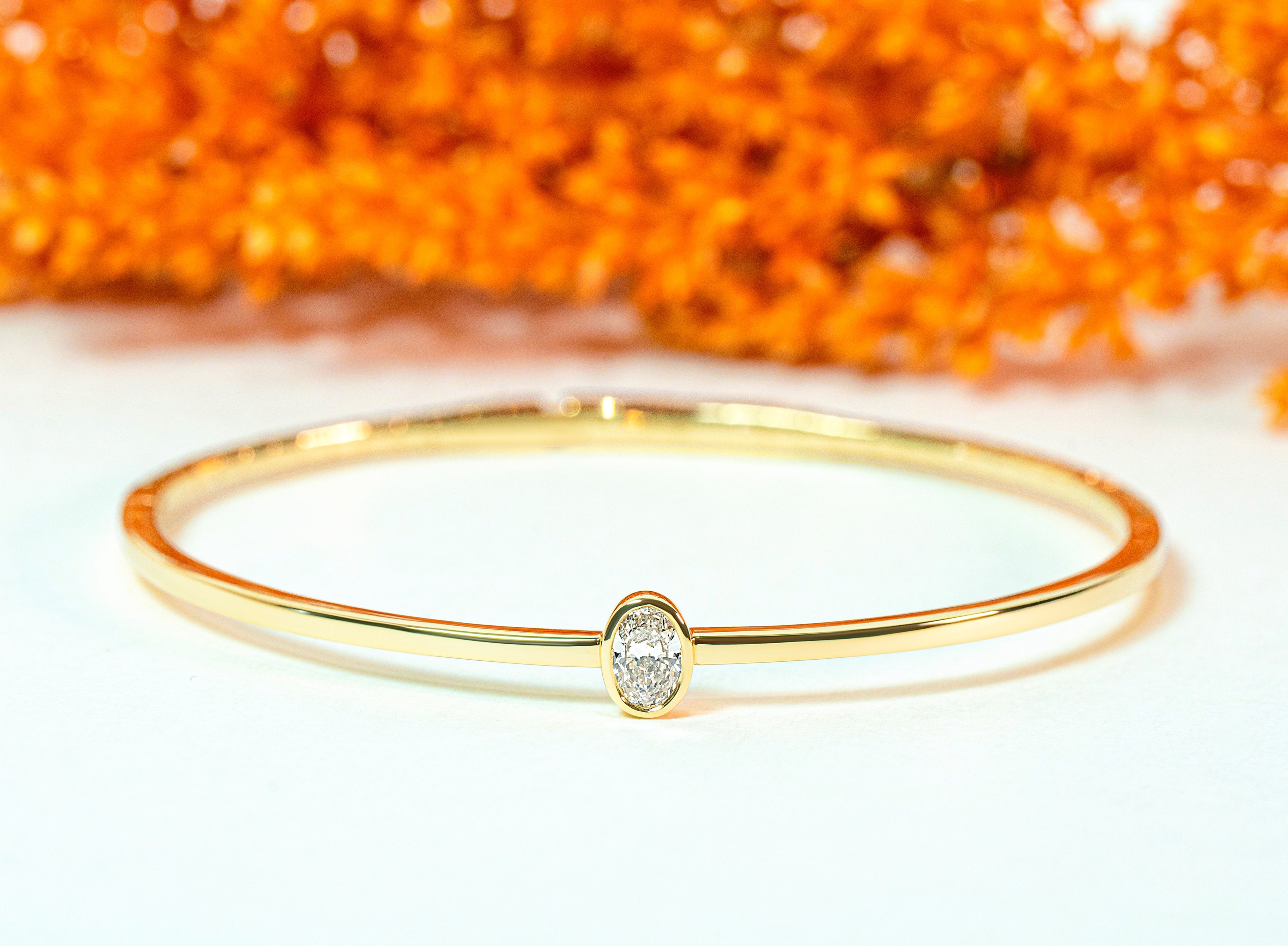Gold bangle with an oval-shaped diamond on an orange background
