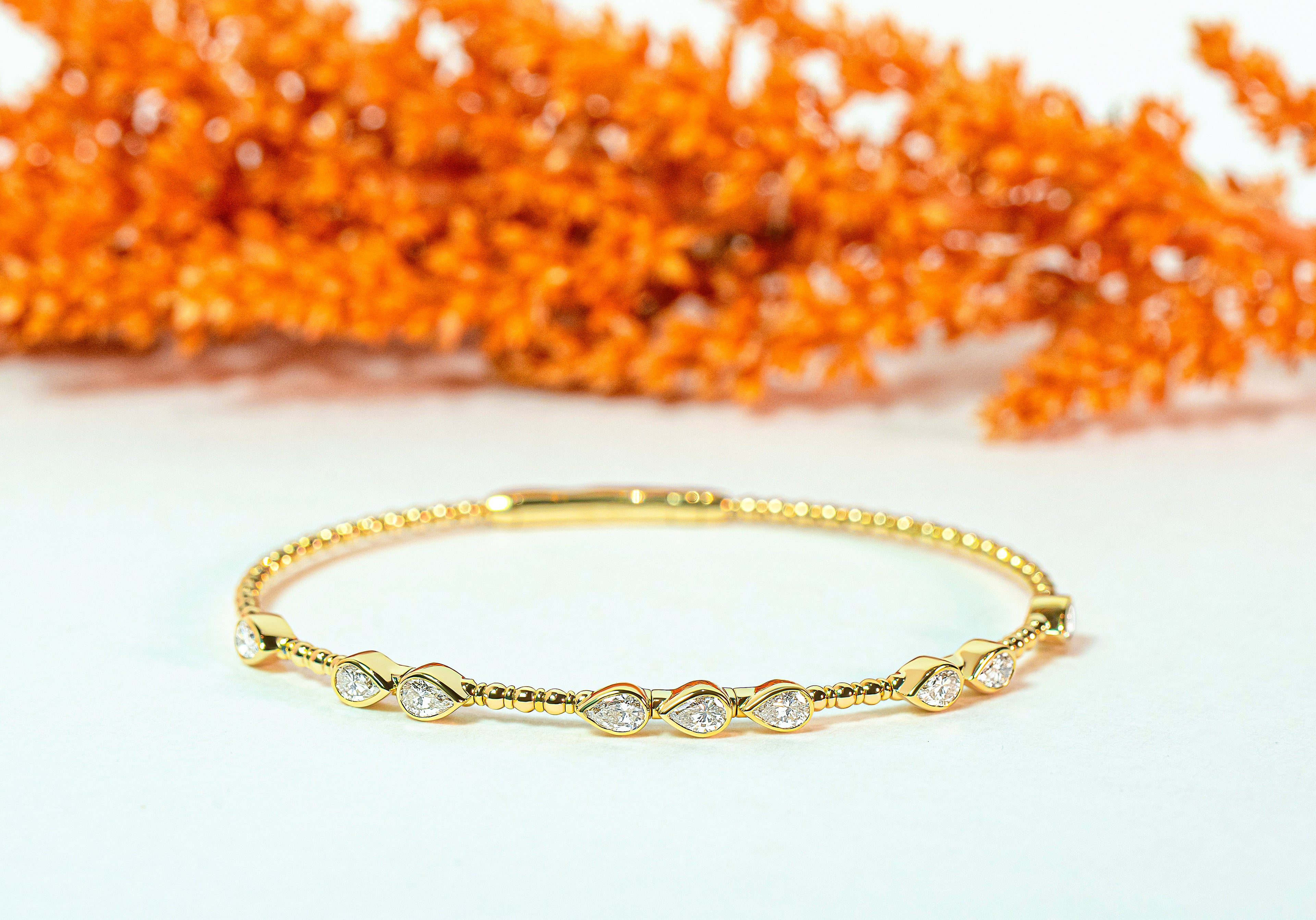 Gold bangle with teardrop or pear-shaped diamonds on a white background with orange decorative elements