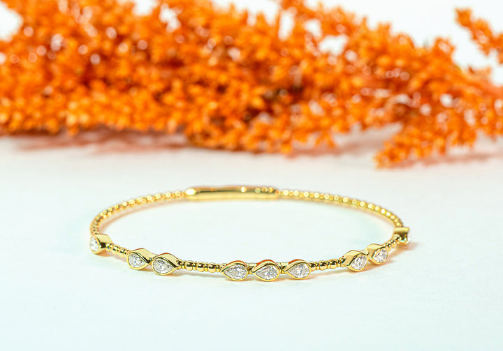 Gold bangle with teardrop or pear-shaped diamonds on a white background with orange decorative elements