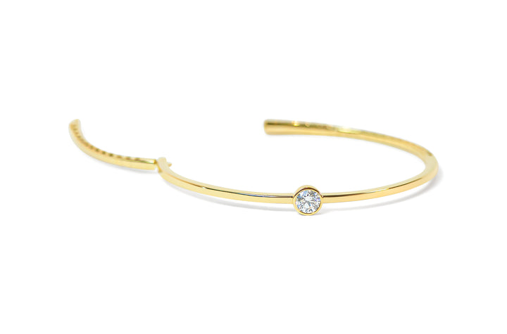 Open gold bangle with a small round diamond on a white background