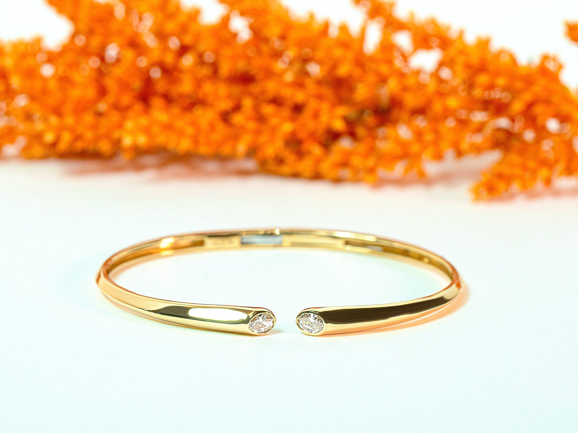 Gold bracelet with two oval diamonds on a white background with orange leaves.