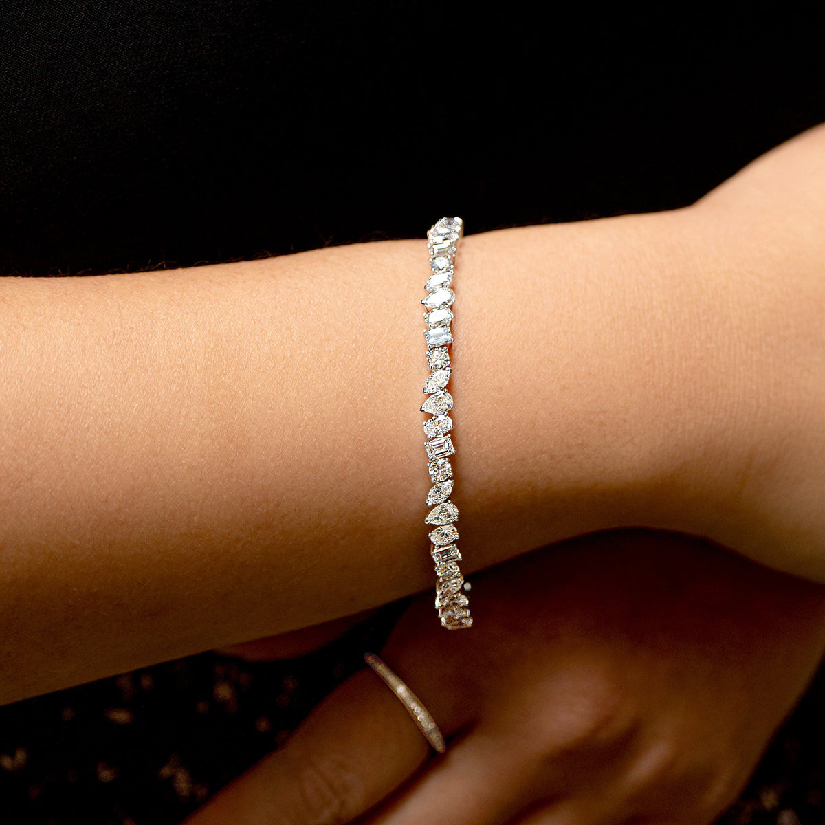 A close-up of a delicate silver mixed-cut diamond tennis bracelet with worn on a woman's wrist, with her hand resting below.