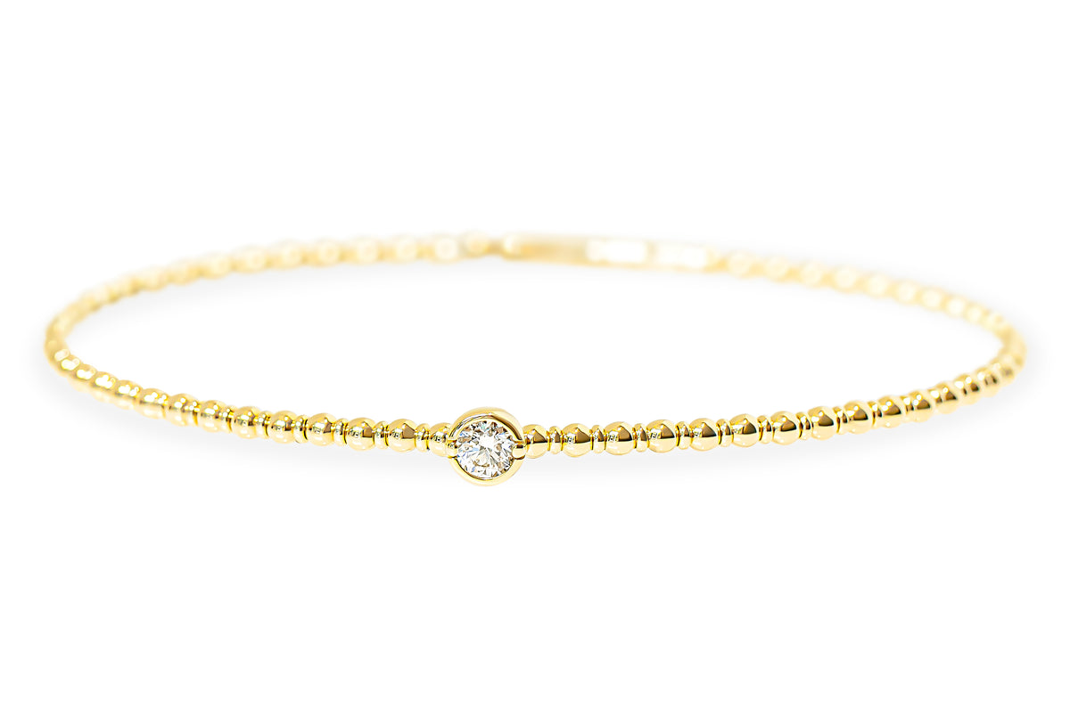 A delicate yellow gold beaded textured bangle with a single bezel-set round diamond at the center, displayed against a clean white background.