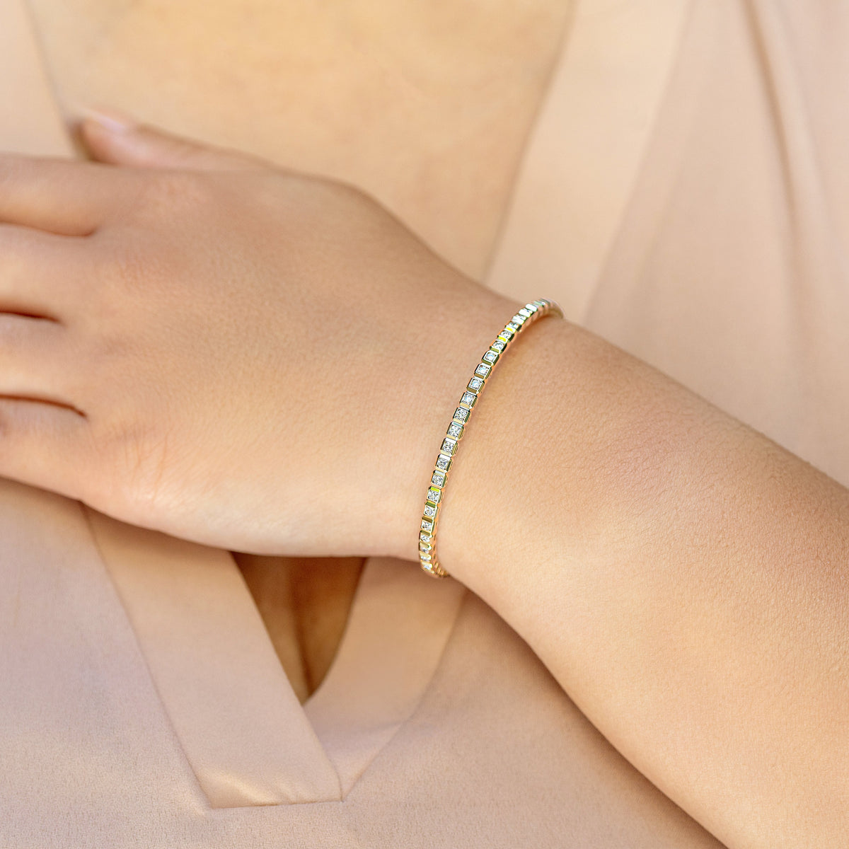 A close-up of a gold diamond bangle with small diamonds worn on a woman's wrist, set against a soft beige blouse.