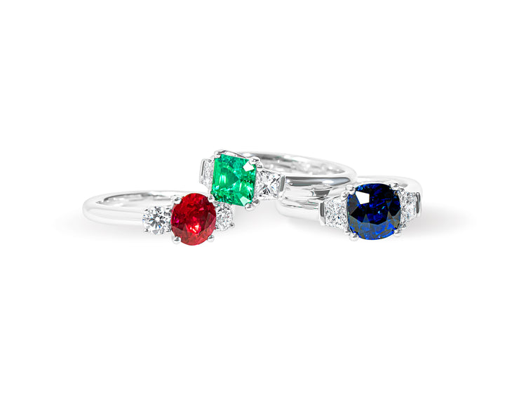 three rings with colored gemstones and diamonds on a white background