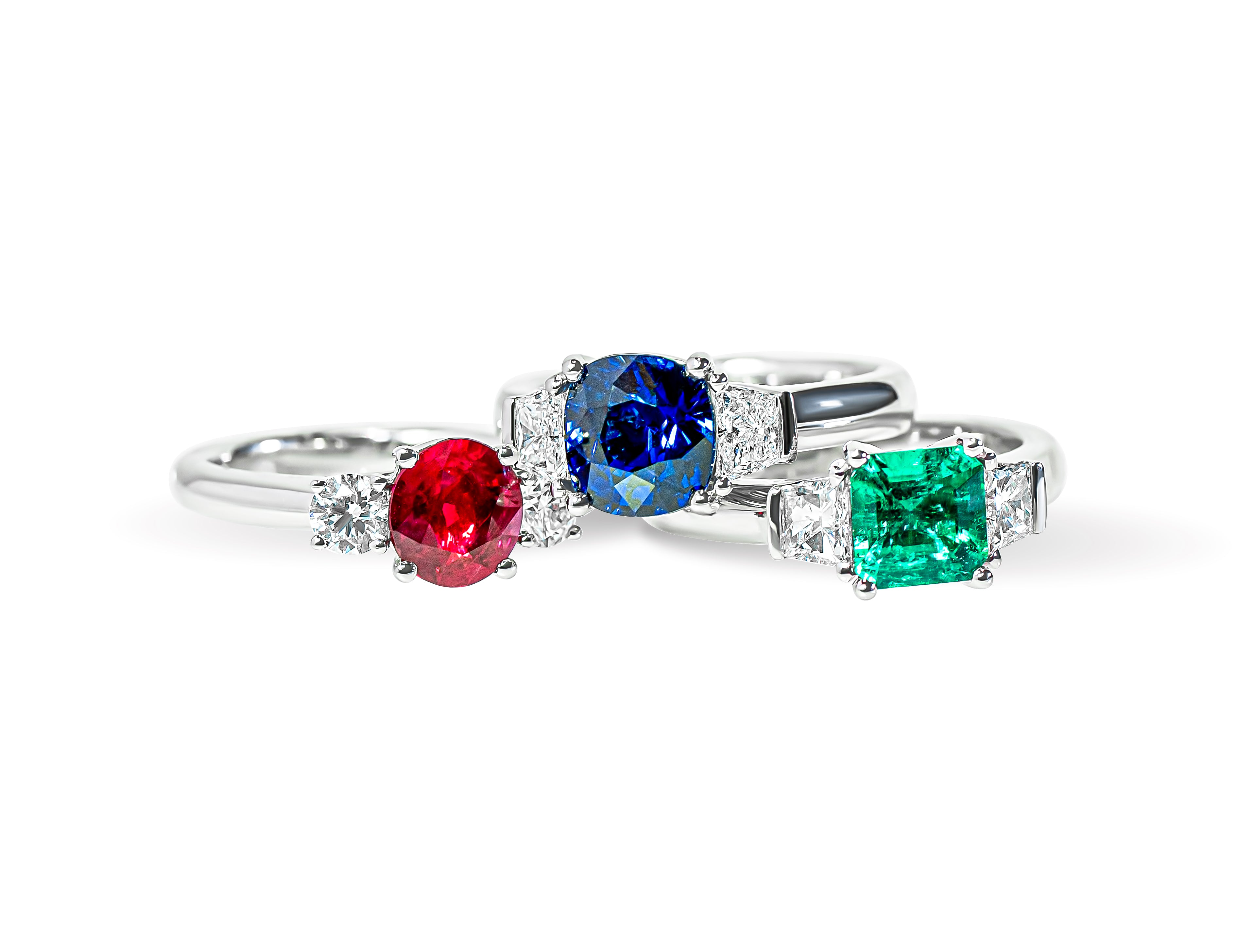 Three rings with colored gemstones and diamonds on a white background