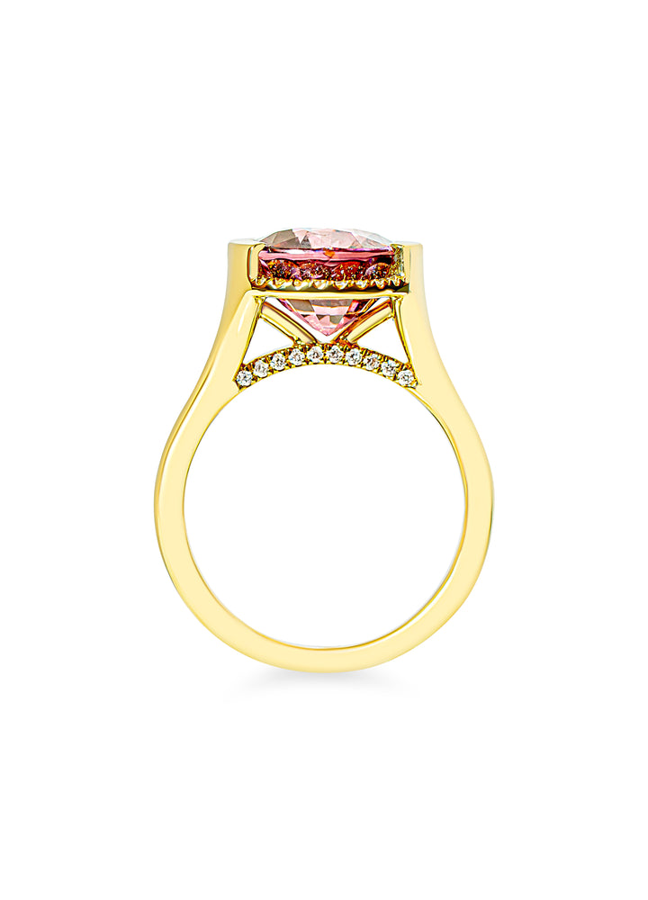 A yellow gold ring featuring a pink gemstone in a half-bezel setting, accented by small diamonds along the bridge, shown on a plain white background.