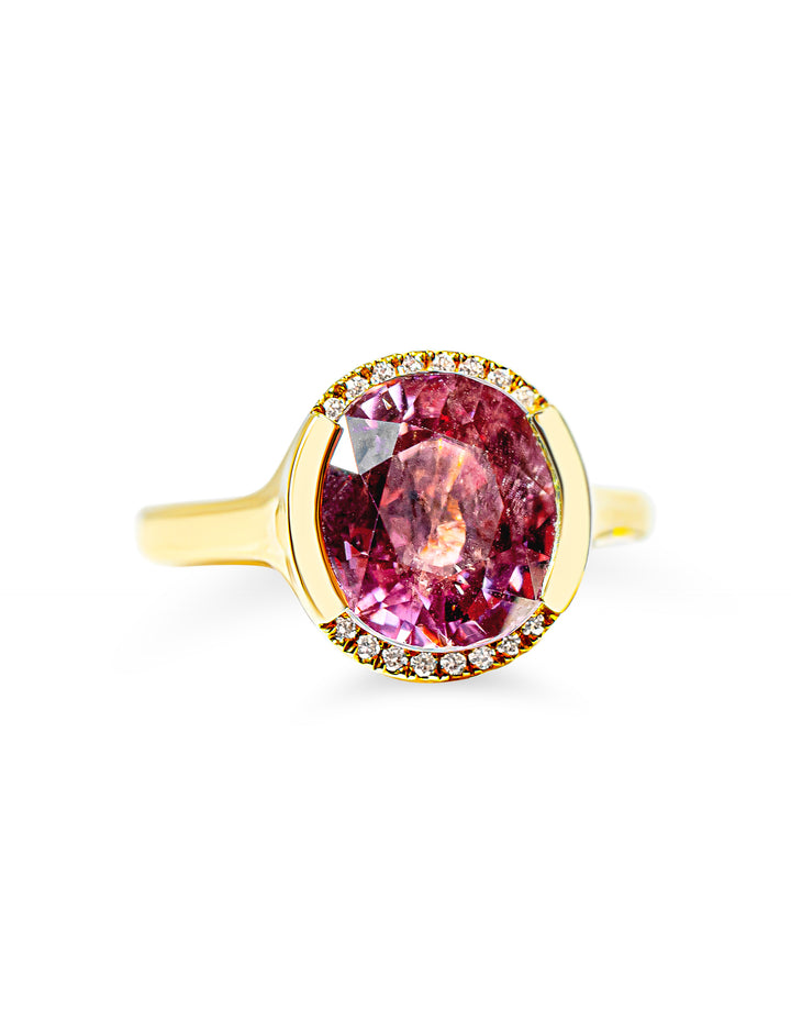 A yellow gold ring featuring a large oval berry pink tourmaline surrounded by a partial halo of diamonds, set against a plain white background.