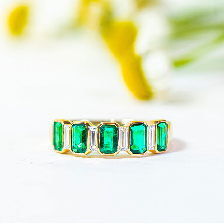 Gold ring with emerald stones on a white background with flowers
