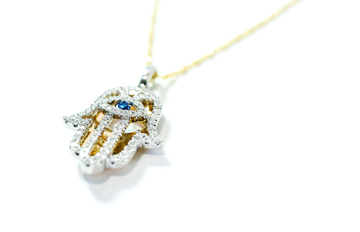 Gold necklace with a hamsa hand pendant featuring a blue gemstone on a white background