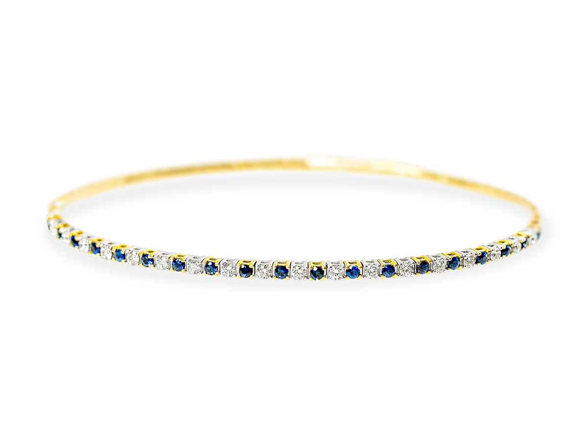 A dainty gold bangle bracelet featuring a continuous row of round-cut blue sapphires and white diamonds, set against a plain white background.