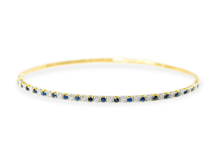 A dainty gold bangle bracelet featuring a continuous row of round-cut blue sapphires and white diamonds, set against a plain white background.