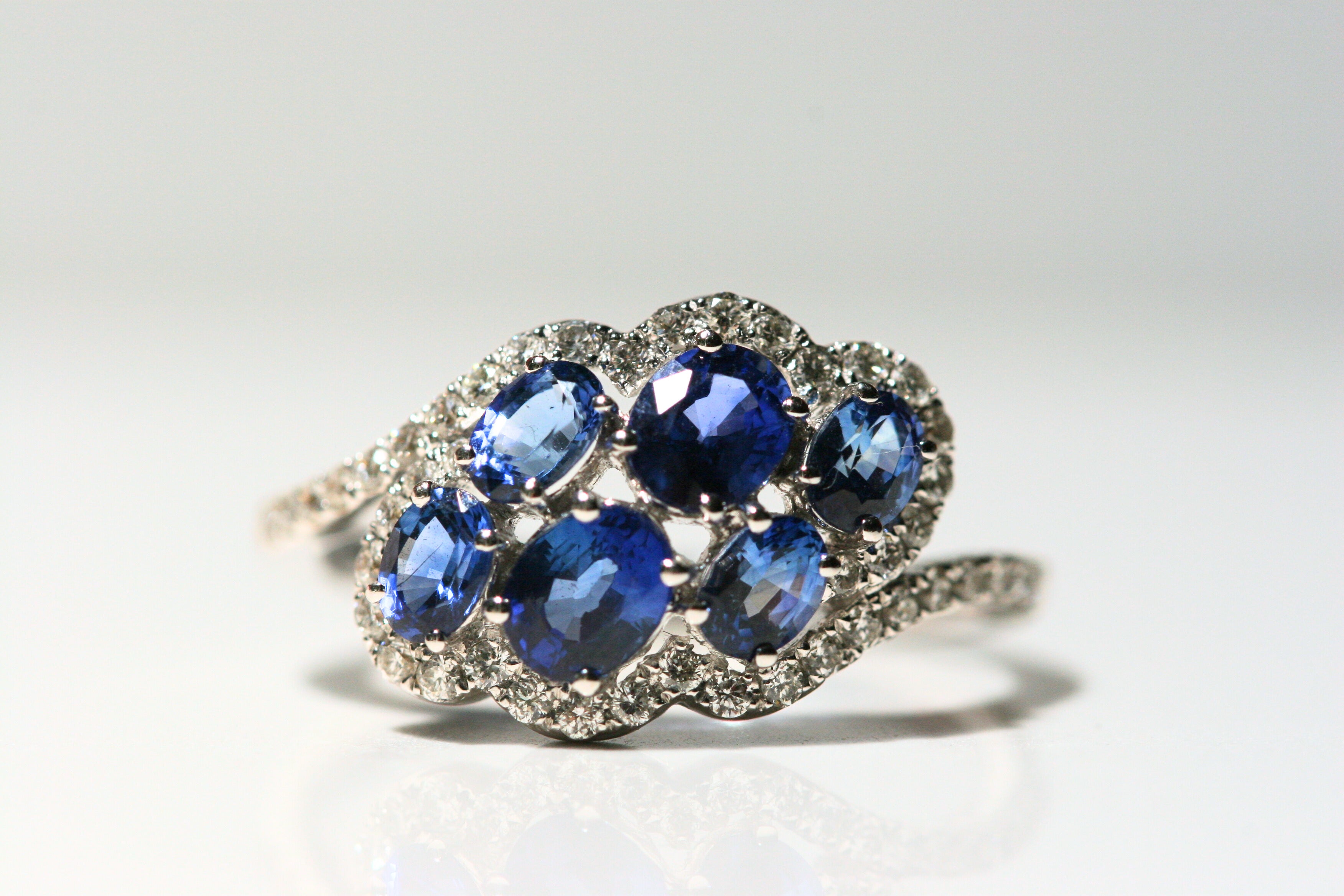 6 oval shaped sapphires float in an abstract, cloud-like shape - surrounded by diamonds. The front of the band is set with diamonds. The back half of the band is solid white gold.