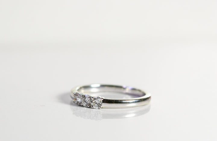 White gold ring with 3 round diamonds in the center. The band is thicker. This photo is a 3/4 view of the ring.