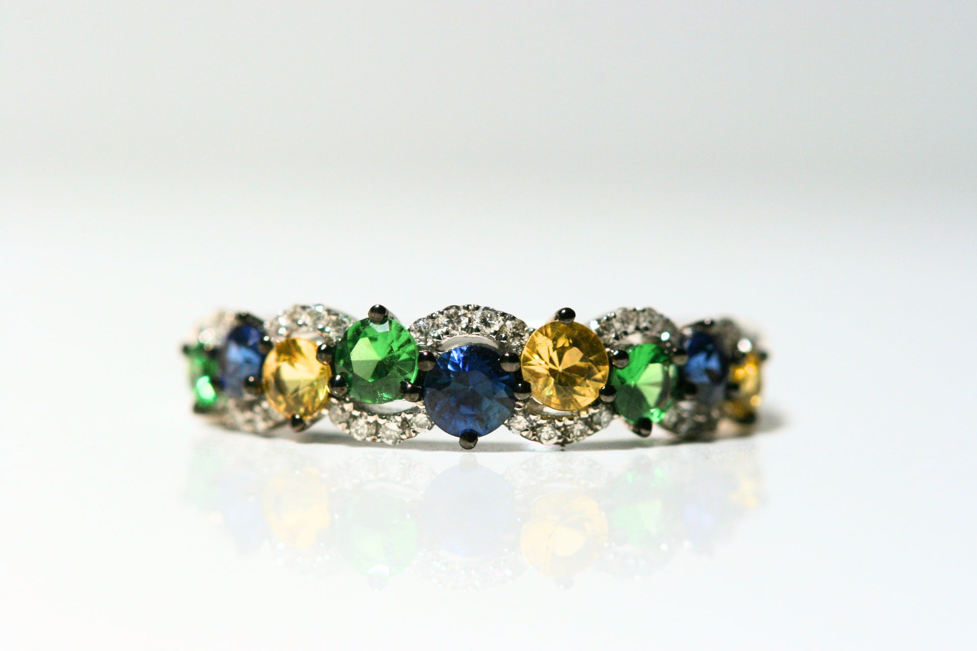 Alternating blue, green, and yellow round stones are framed by curves of white diamonds. All set in white gold - and the prongs are plated in black rhodium.