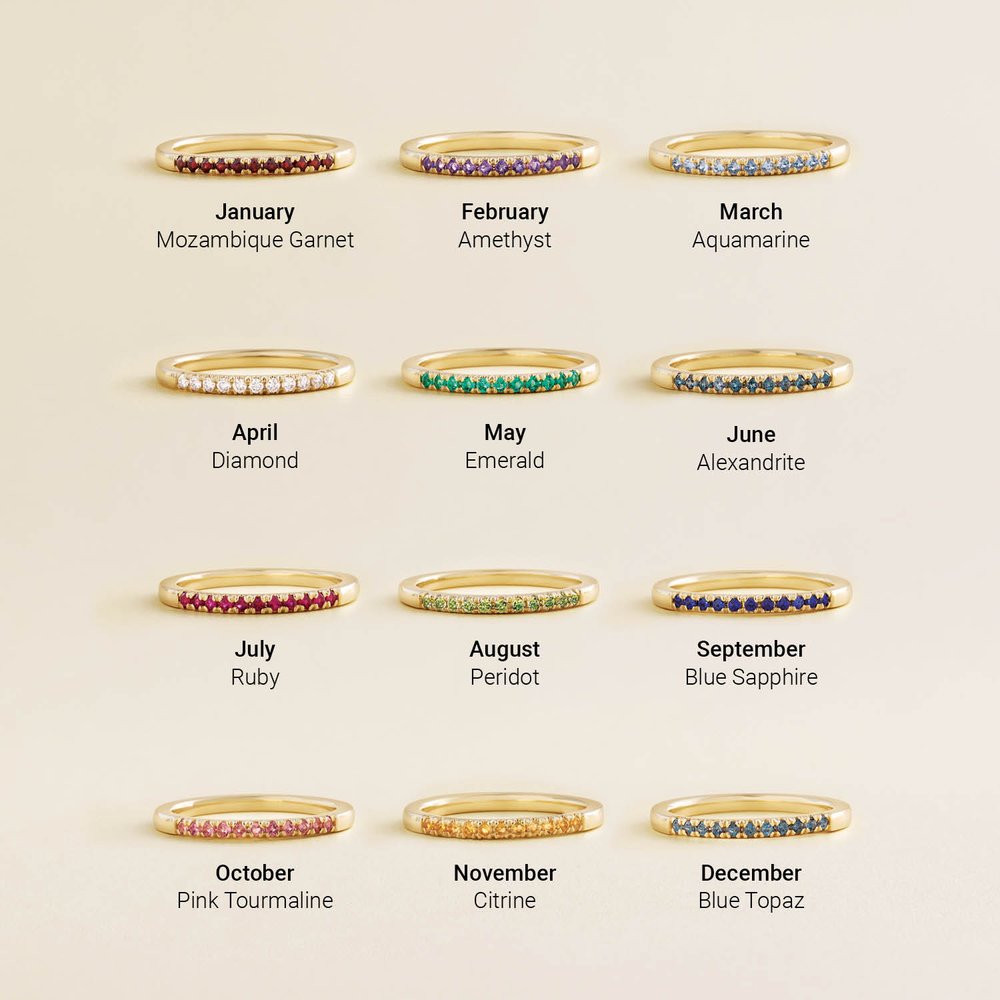 Gold rings with gemstones for each month, on a beige background