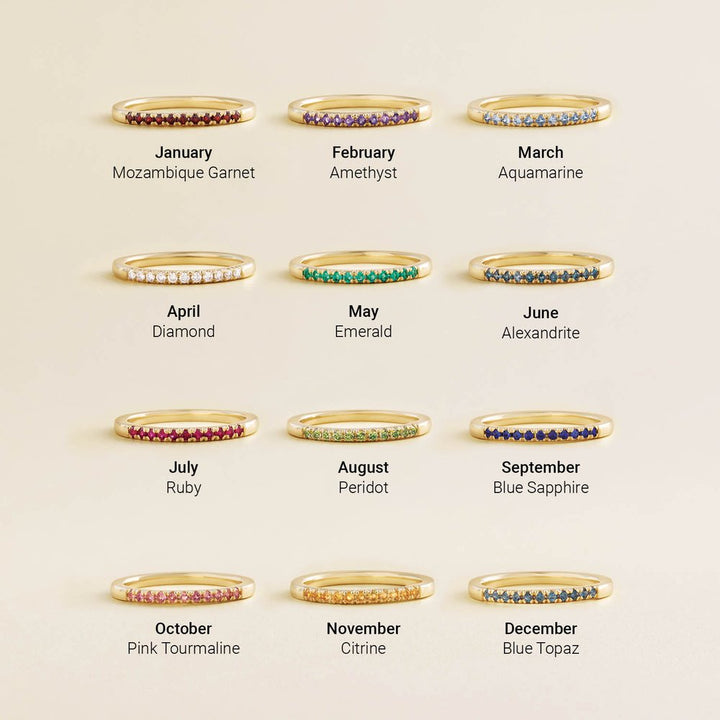 Gold rings with gemstones for each month, on a beige background