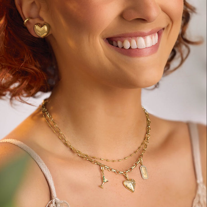 Woman wearing gold jewelry with a necklace and earrings on a neutral background