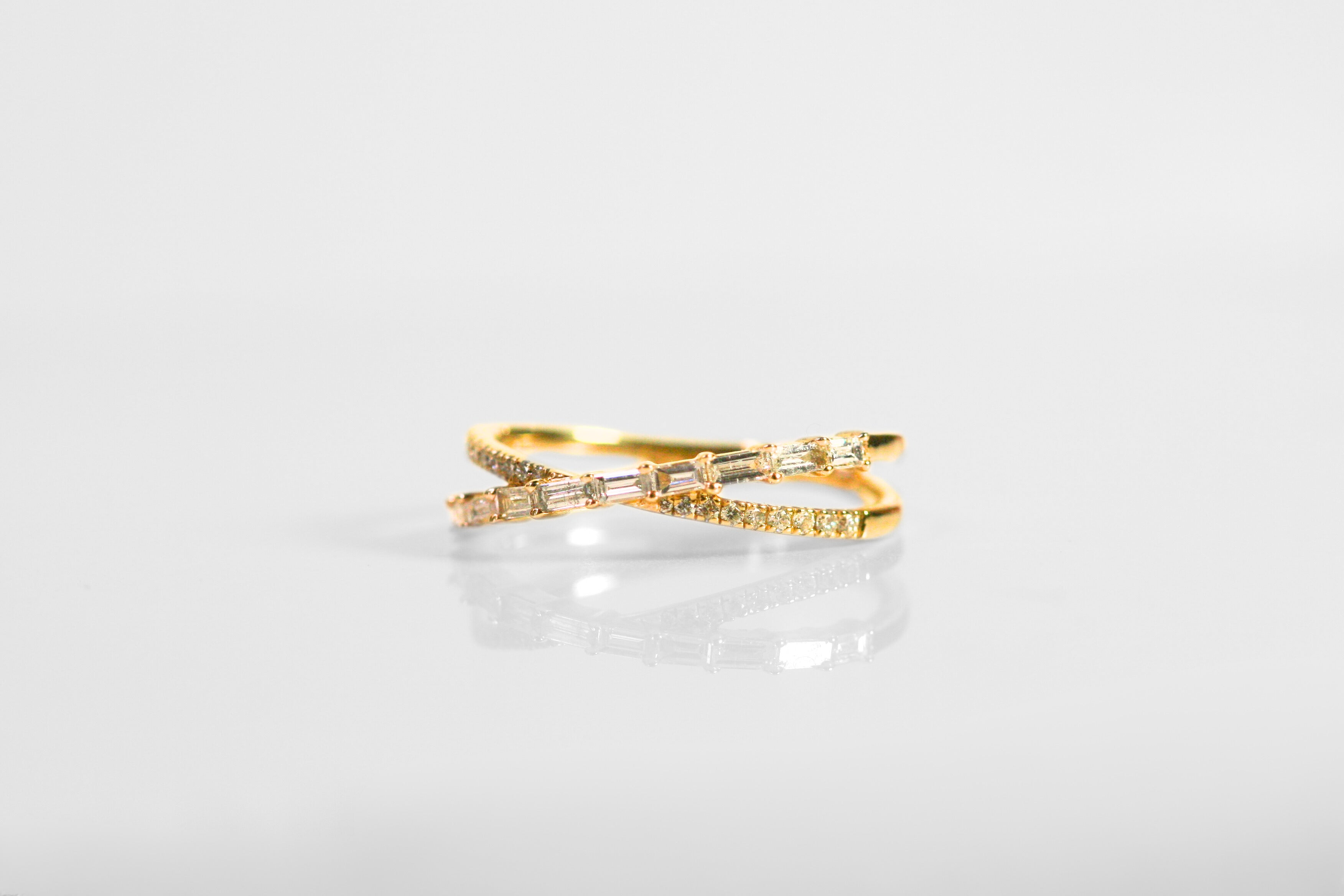 Ring shaped like an X. One arm of the X has round, brilliant cut diamonds. The other has horizontal baguettes. Set in yellow gold.