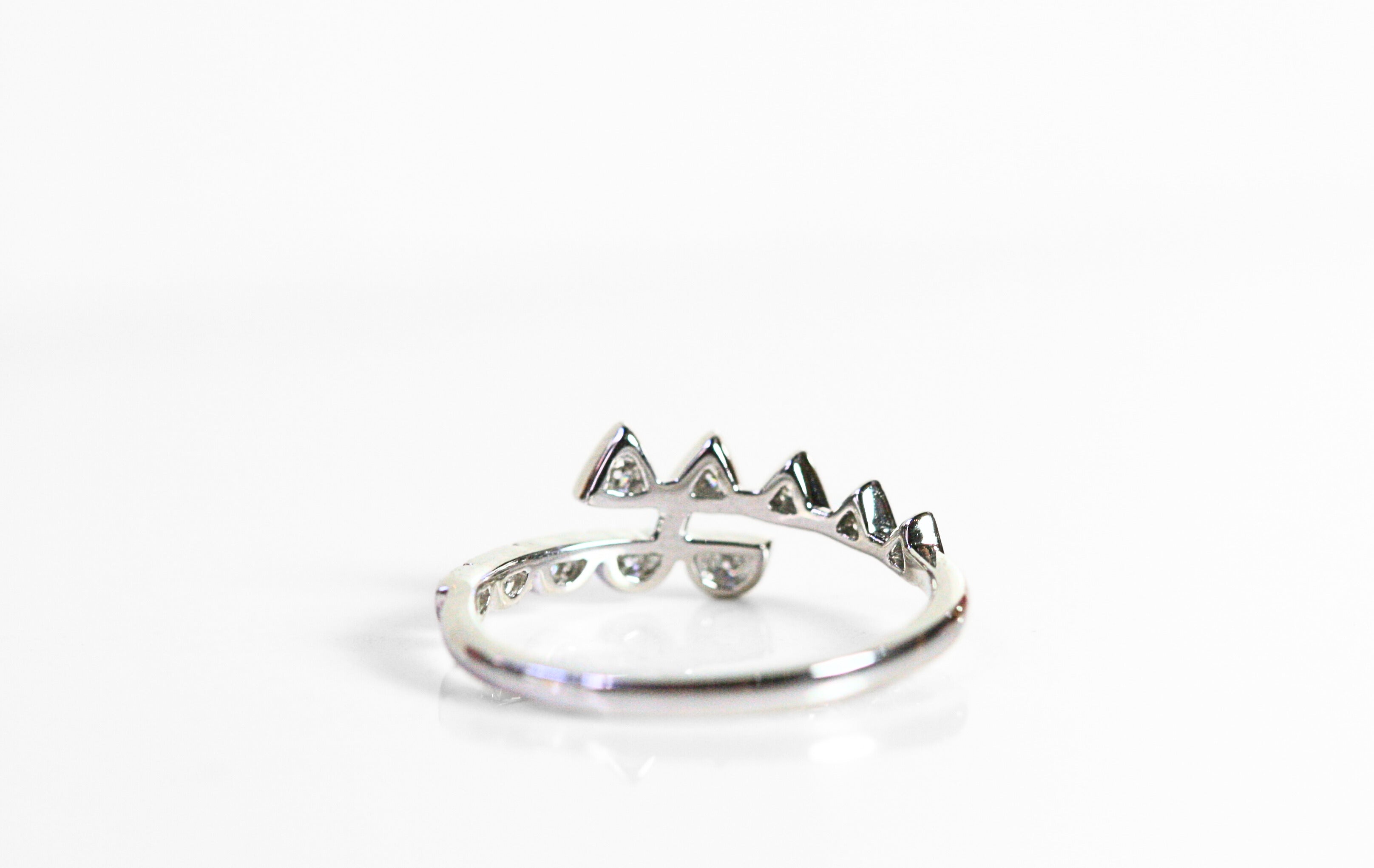 White gold ring with diamonds. Two arms wrap around the finger. Diamond triangles are on one arm, and half circles are on the other.