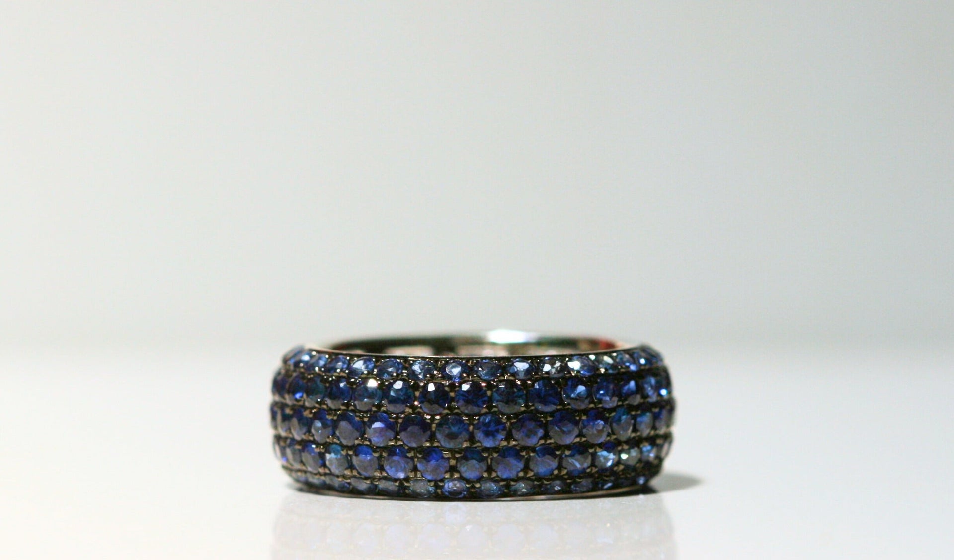 Thick band ring. Covered in round, deep blue sapphires, which graduate in size from the top and bottom towards the center. Set in black rhodium plated white gold. 