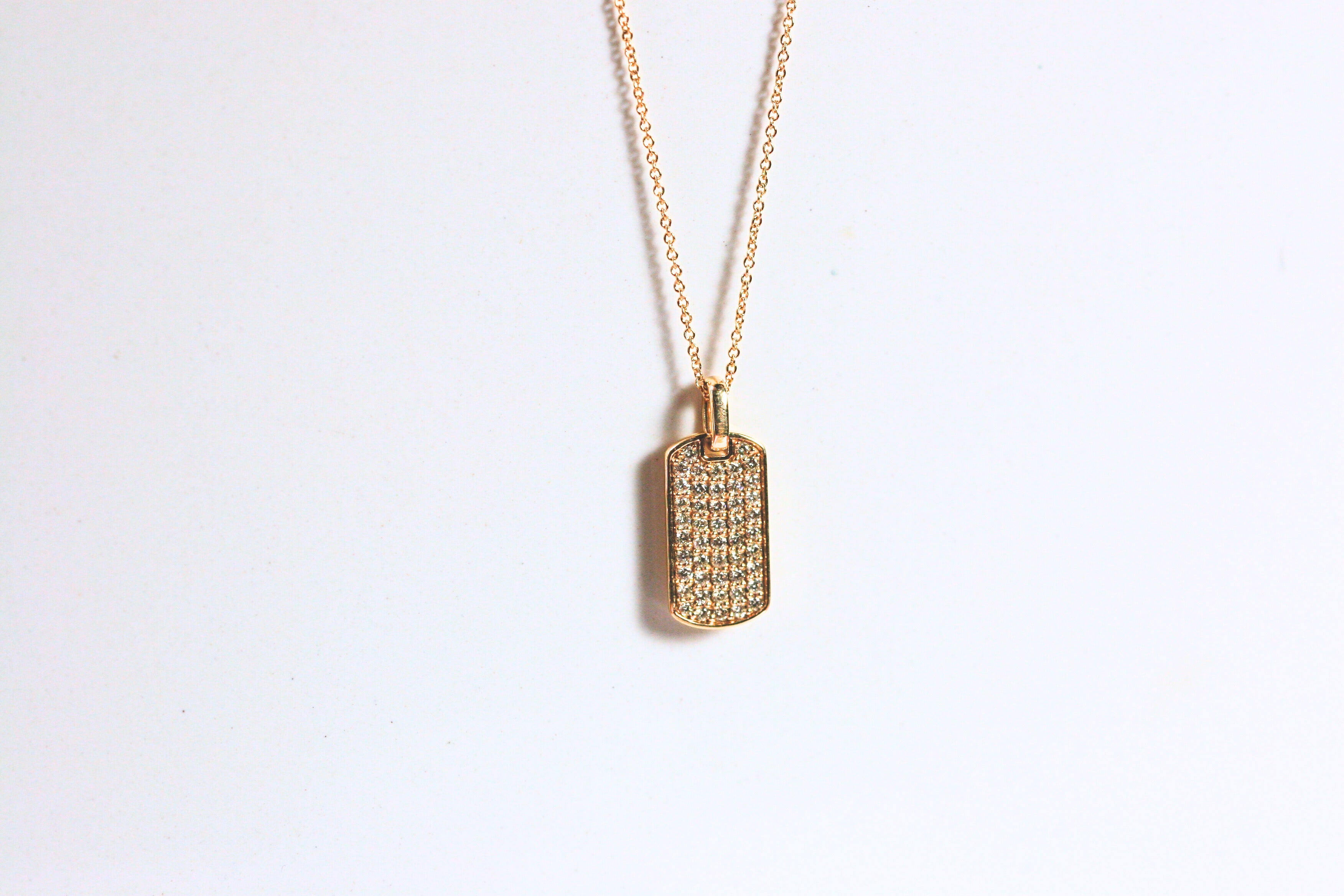 Yellow gold dog tag is pave set with diamonds. A thick gold bail allows the pendant to hang from a yellow gold rolo chain.