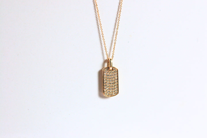 Yellow gold dog tag is pave set with diamonds. A thick gold bail allows the pendant to hang from a yellow gold rolo chain.