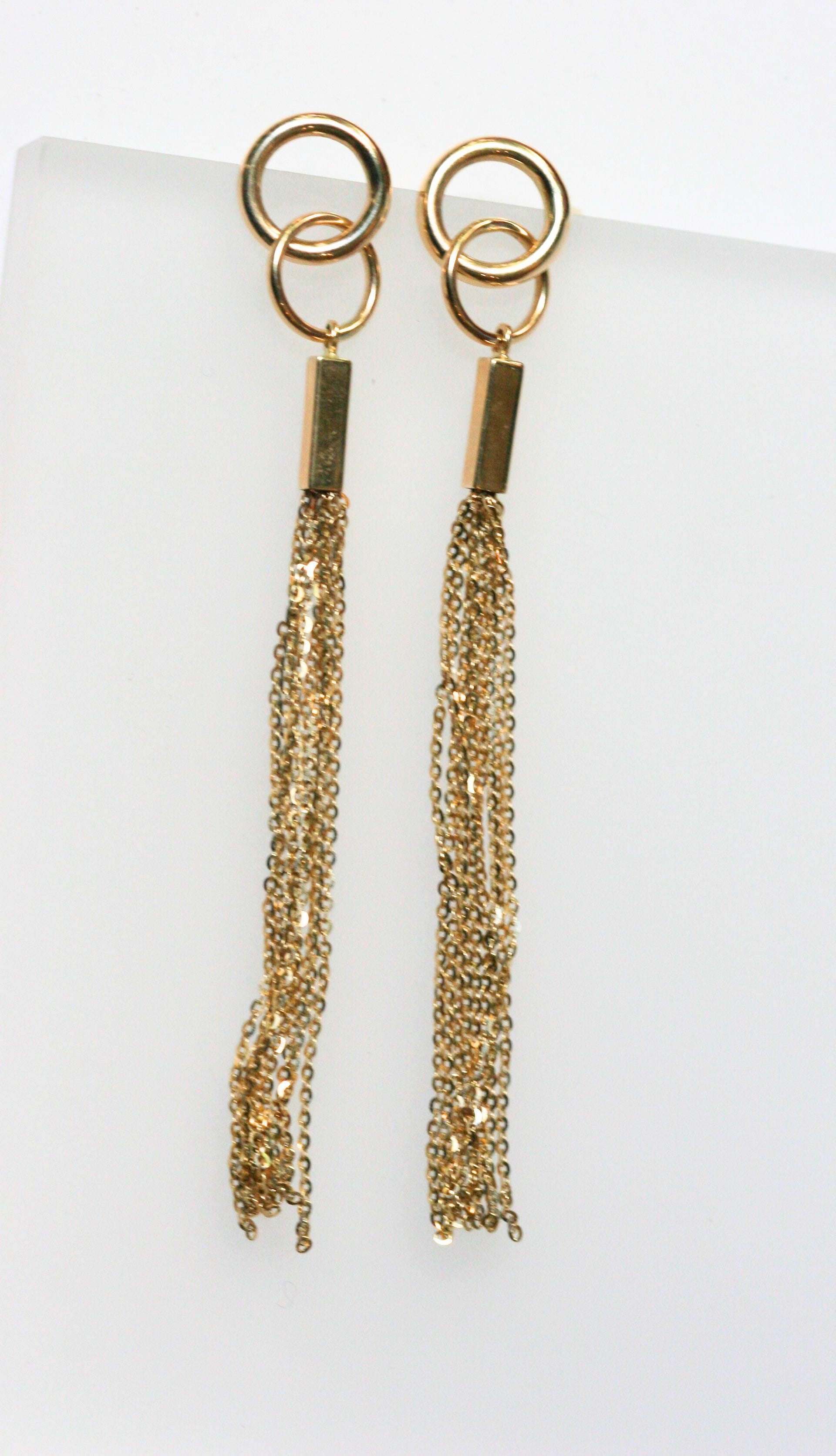 Long gold earrings. Two interlocking circles sit on the ear, while long gold chains dangle off the lower circle.