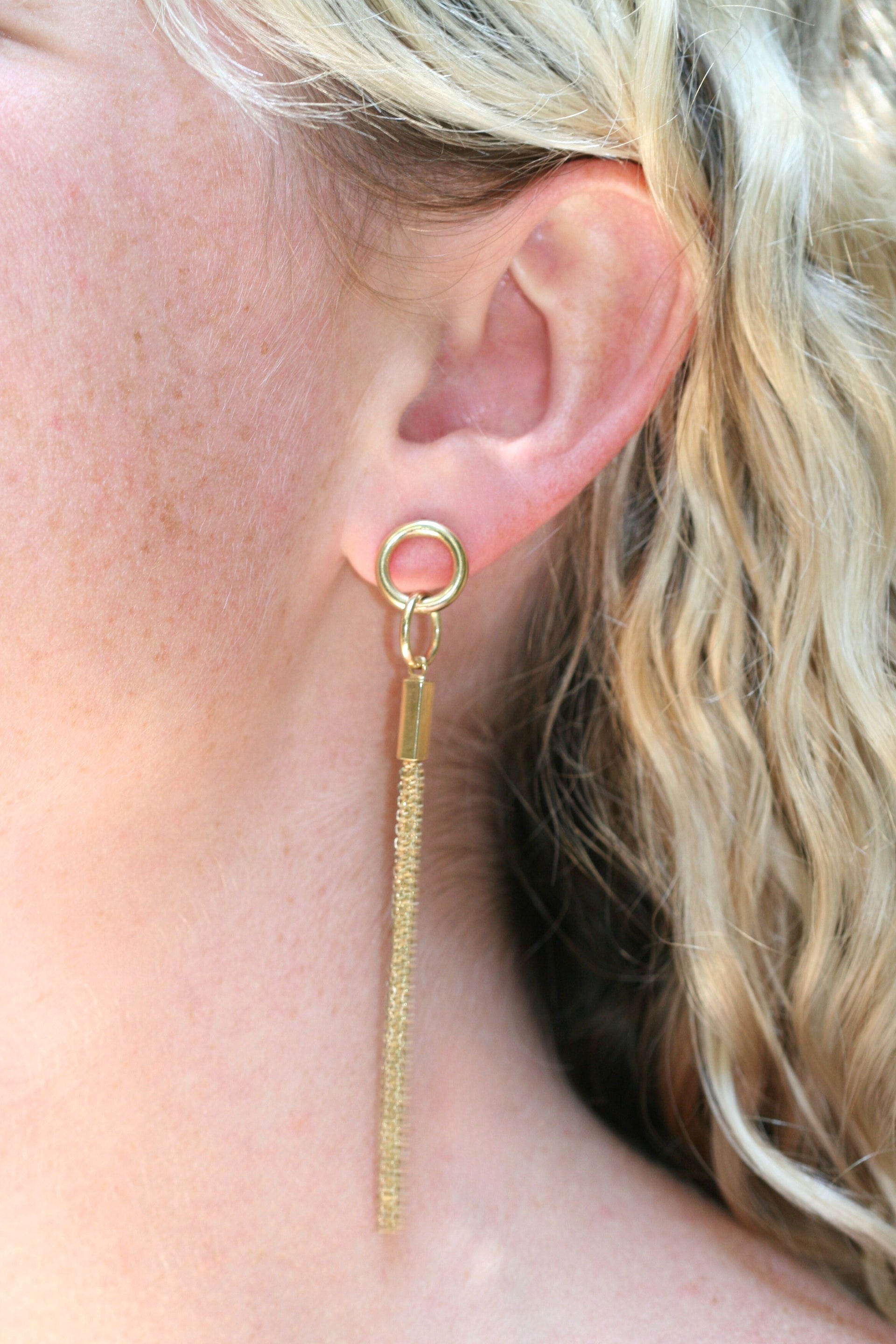 Long gold earrings. Two interlocking circles sit on the ear, while long gold chains dangle off the lower circle.