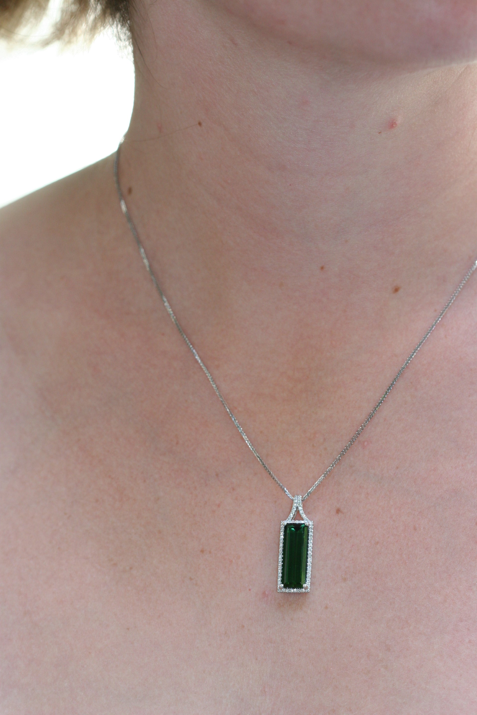 Green rectangle stone. Dark green. Surrounded by diamonds, set in white gold. On white gold chain.