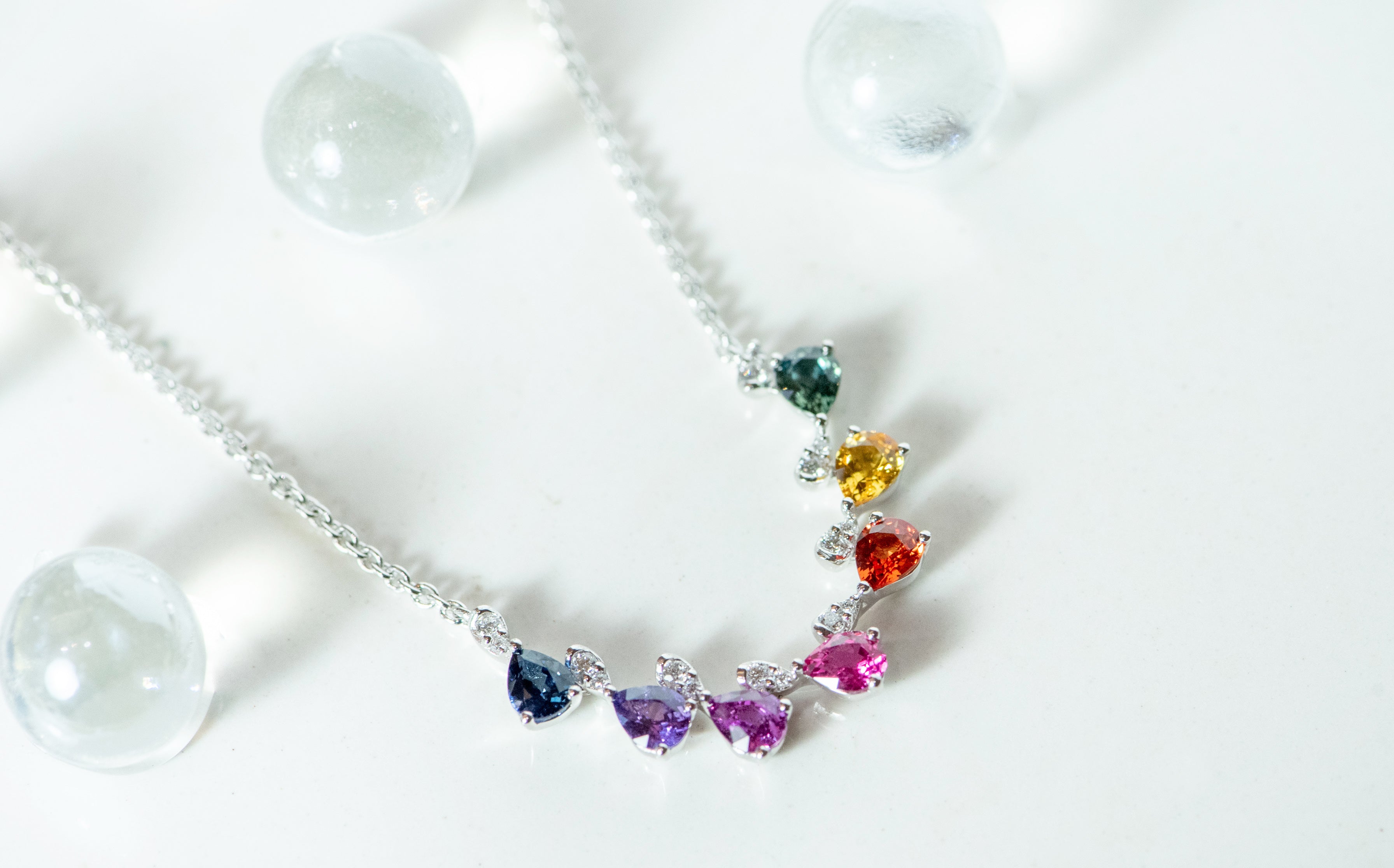 Rainbow sapphires - pear shaped. Offset by diamonds. In white gold with white gold chain. Blue sapphire, purple sapphires, pink sapphire, orange sapphire, yellow sapphire, and green sapphire.