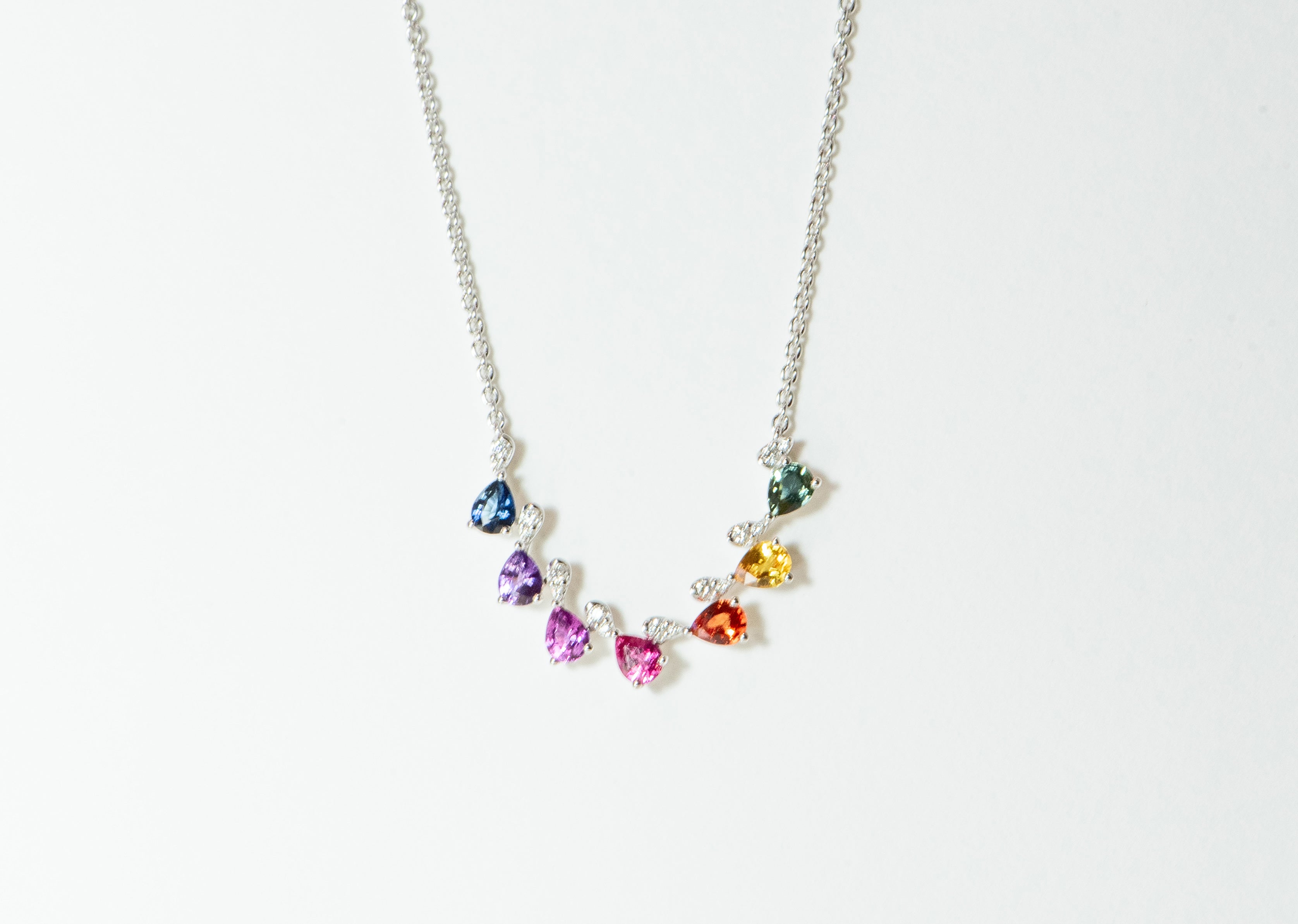 Rainbow sapphires - pear shaped. Offset by diamonds. In white gold with white gold chain. Blue sapphire, purple sapphires, pink sapphire, orange sapphire, yellow sapphire, and green sapphire.